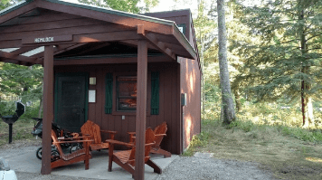 A mini cabin at a park with chairs under the awning
