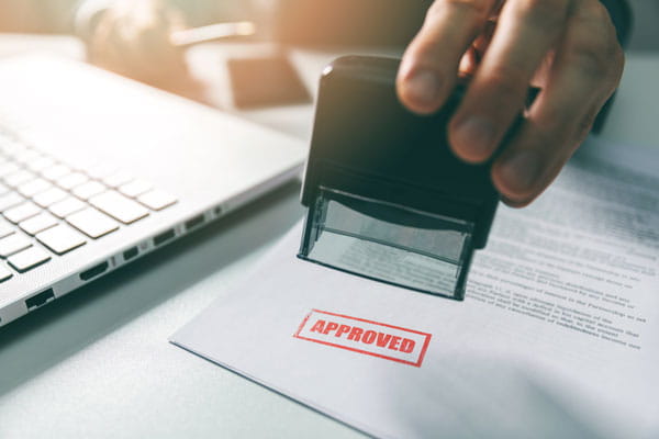 A person stamps the word approved onto some paperwork. 