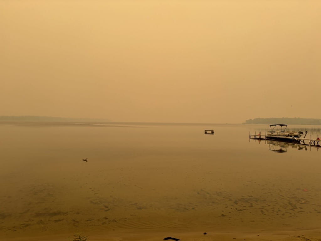 An eerie yellow haze settles over the still waters of Big Manistique Lake during a wildfire smoke event