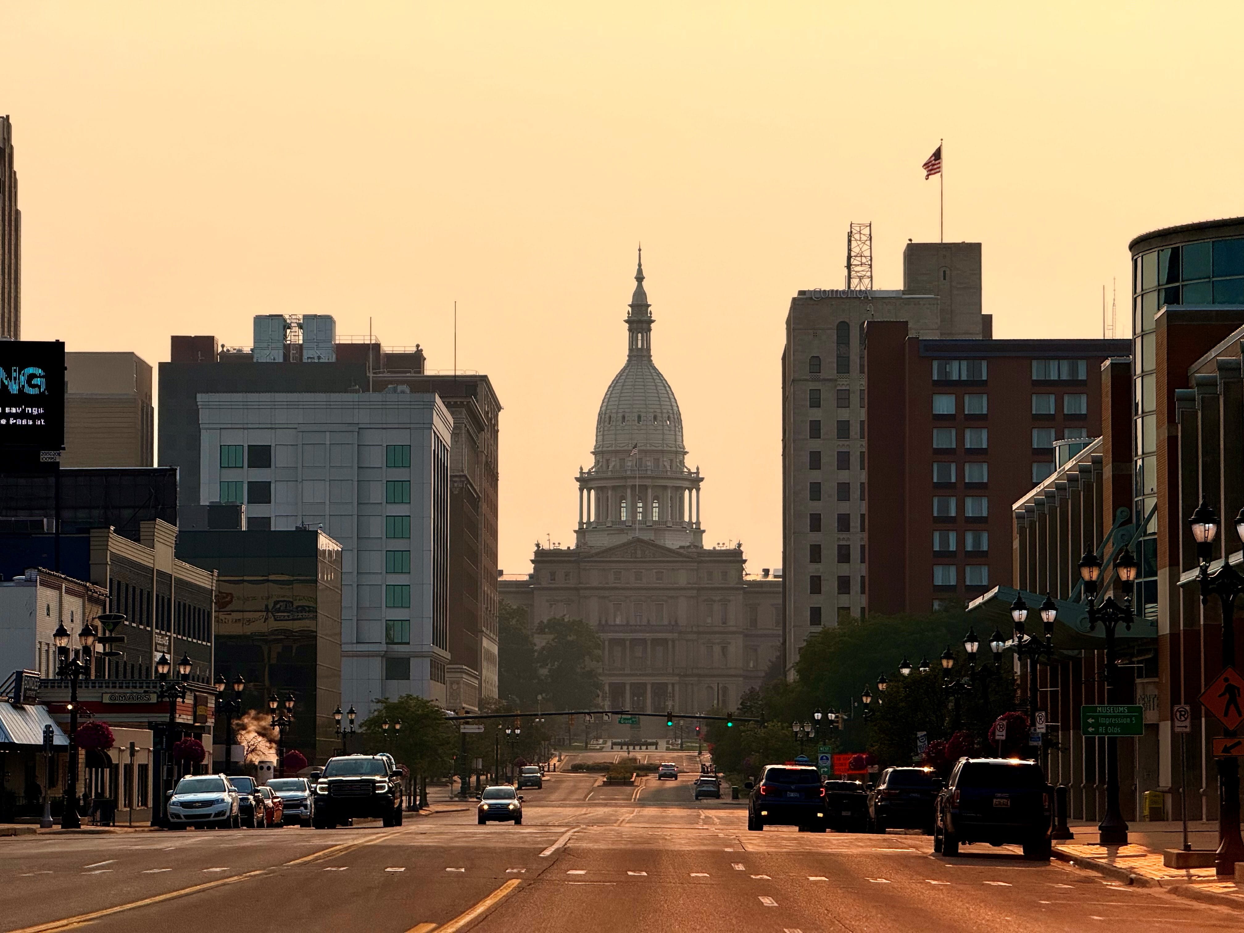 A street-level view of the Michigan State Capitol building in Lansing with smoky air and a warm orange hue from wildfire smoke