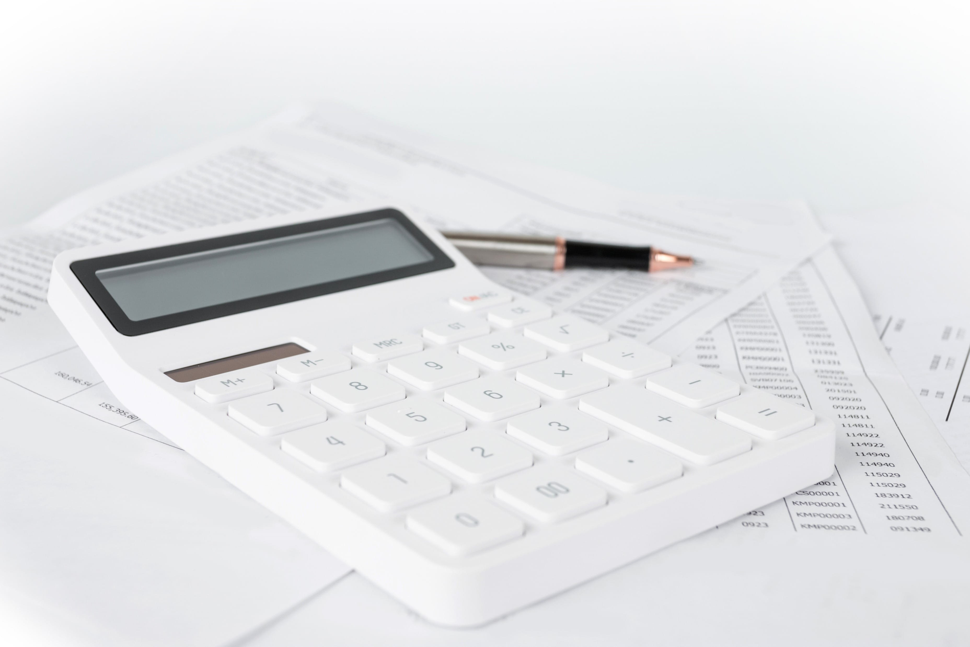a calculator sitting atop paperwork aside a pen