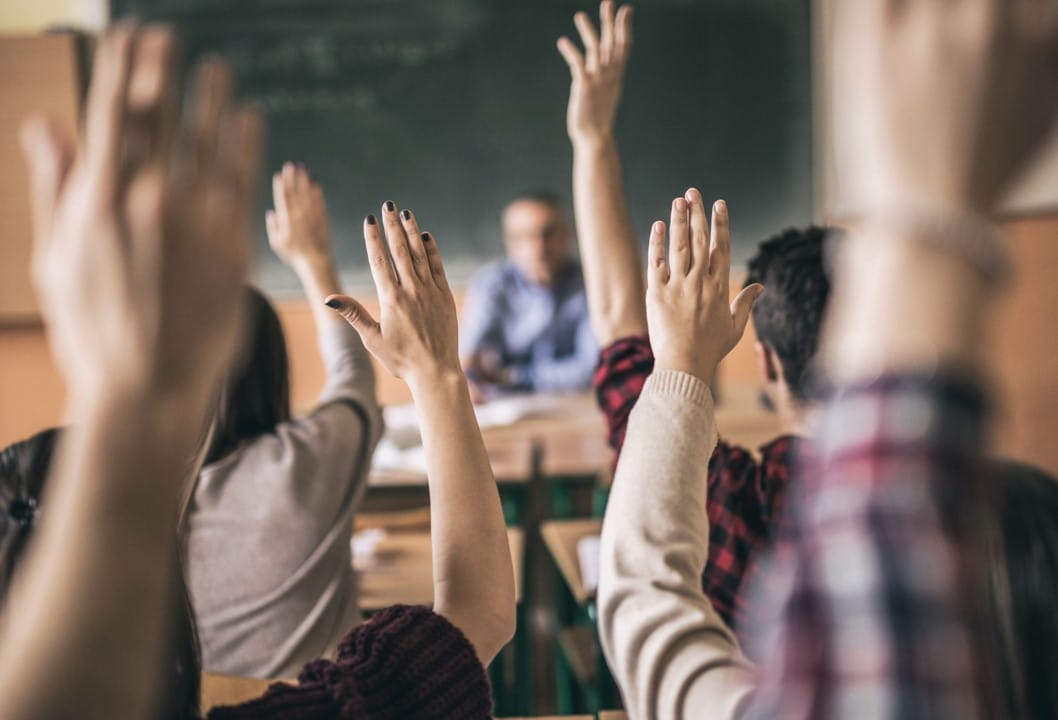 students raise their hands in a classroom