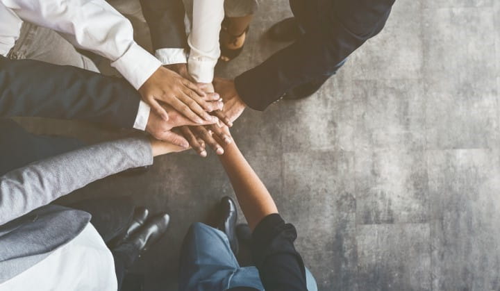 A group of people placing their hands together in a circle as to say, "Go team!"