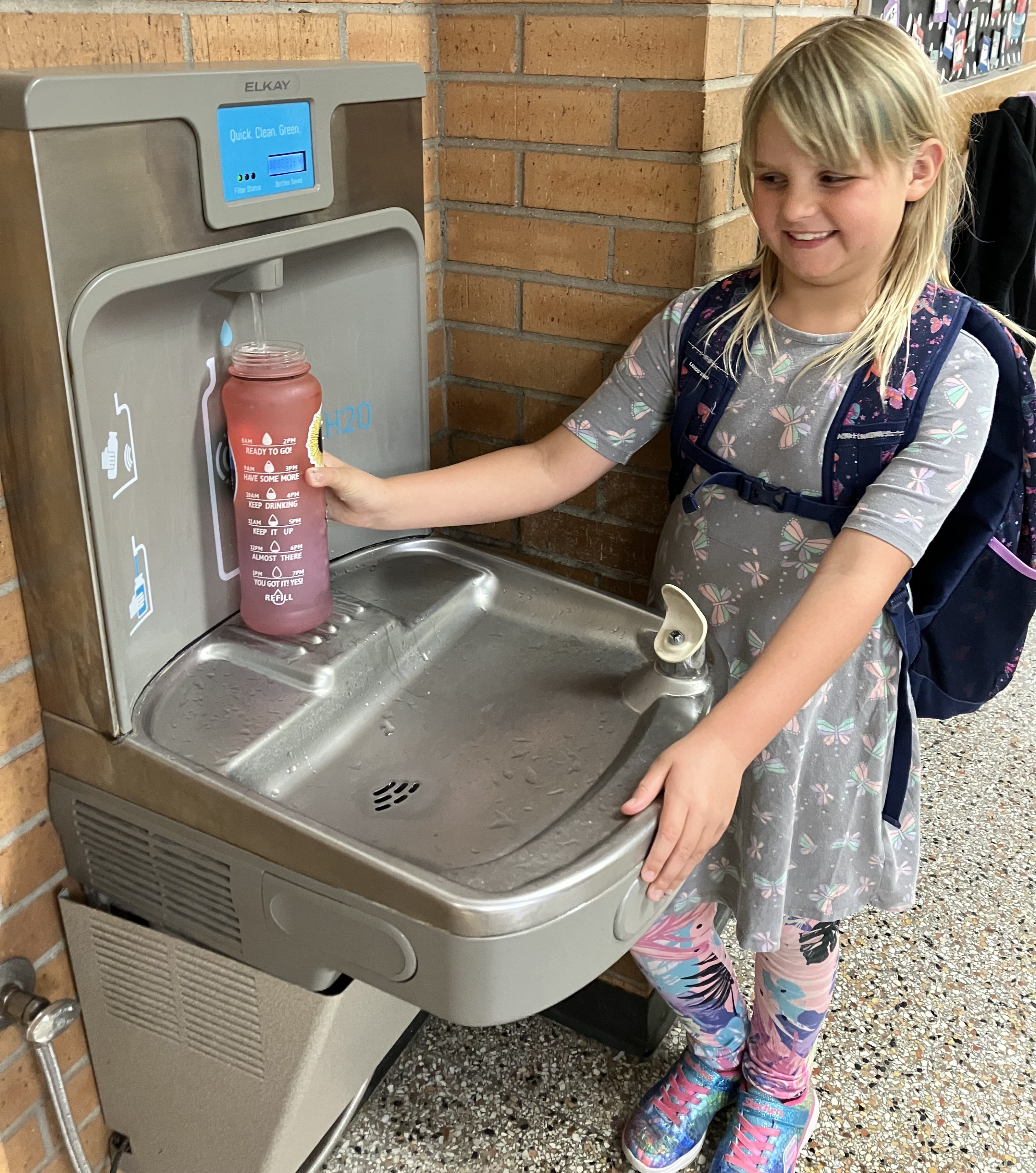 Girl filling water bottle from water fountain with filtered water.