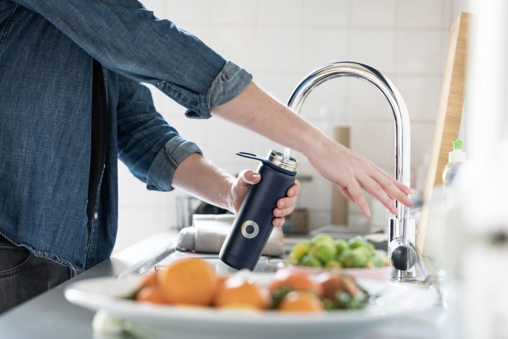 A person filling a black metal water bottle at a kitchen sink