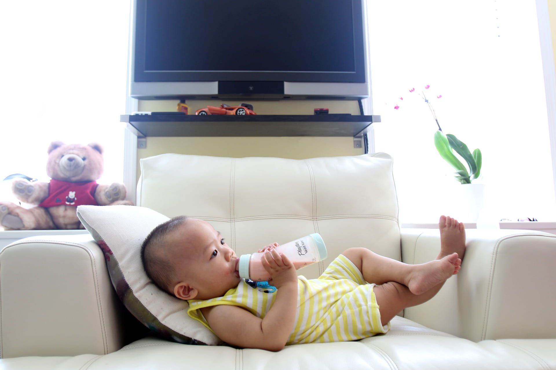 baby drinking formula or milk out of a bottle, laying on the couch