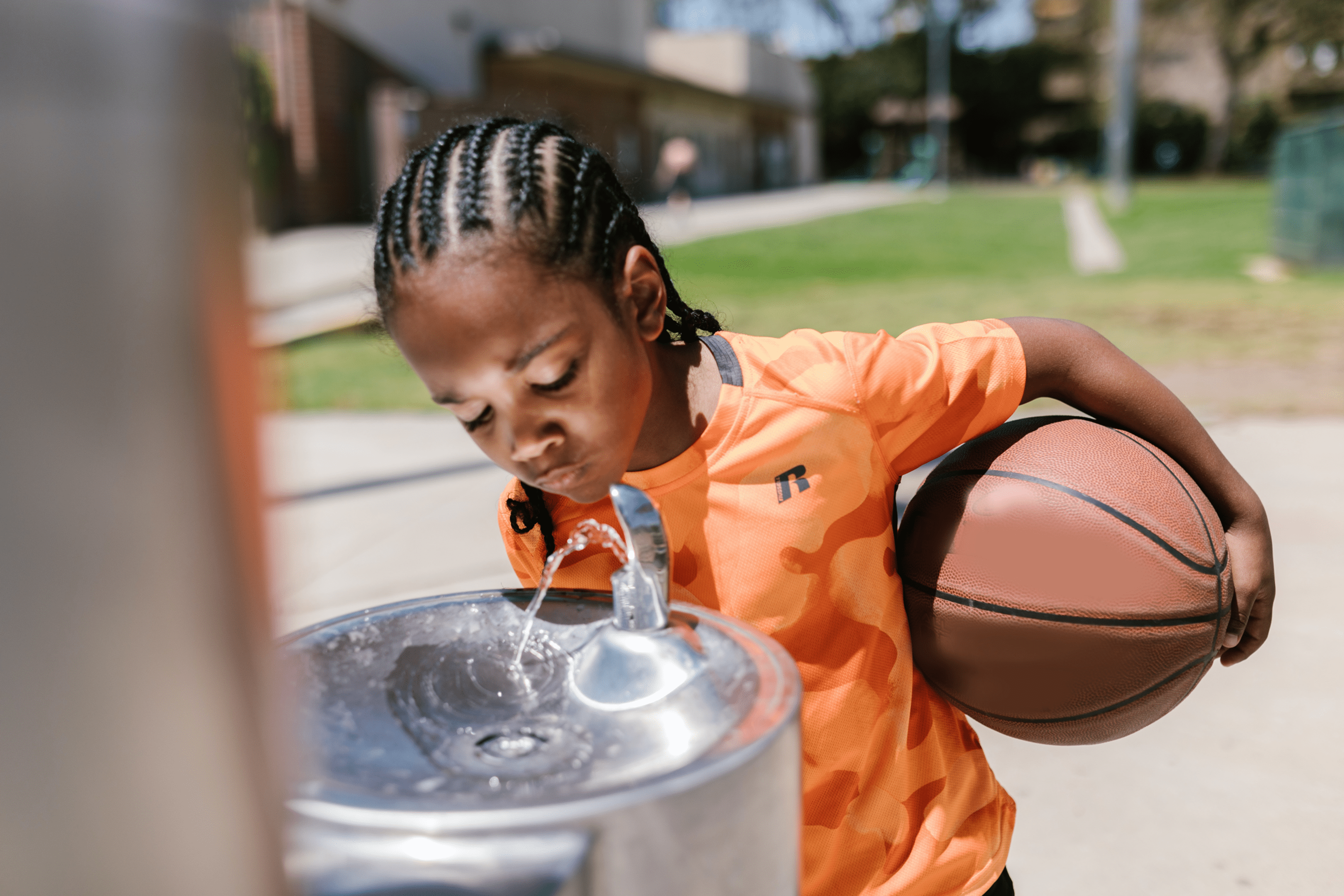 boy drinking from water fountain with basketball under arm