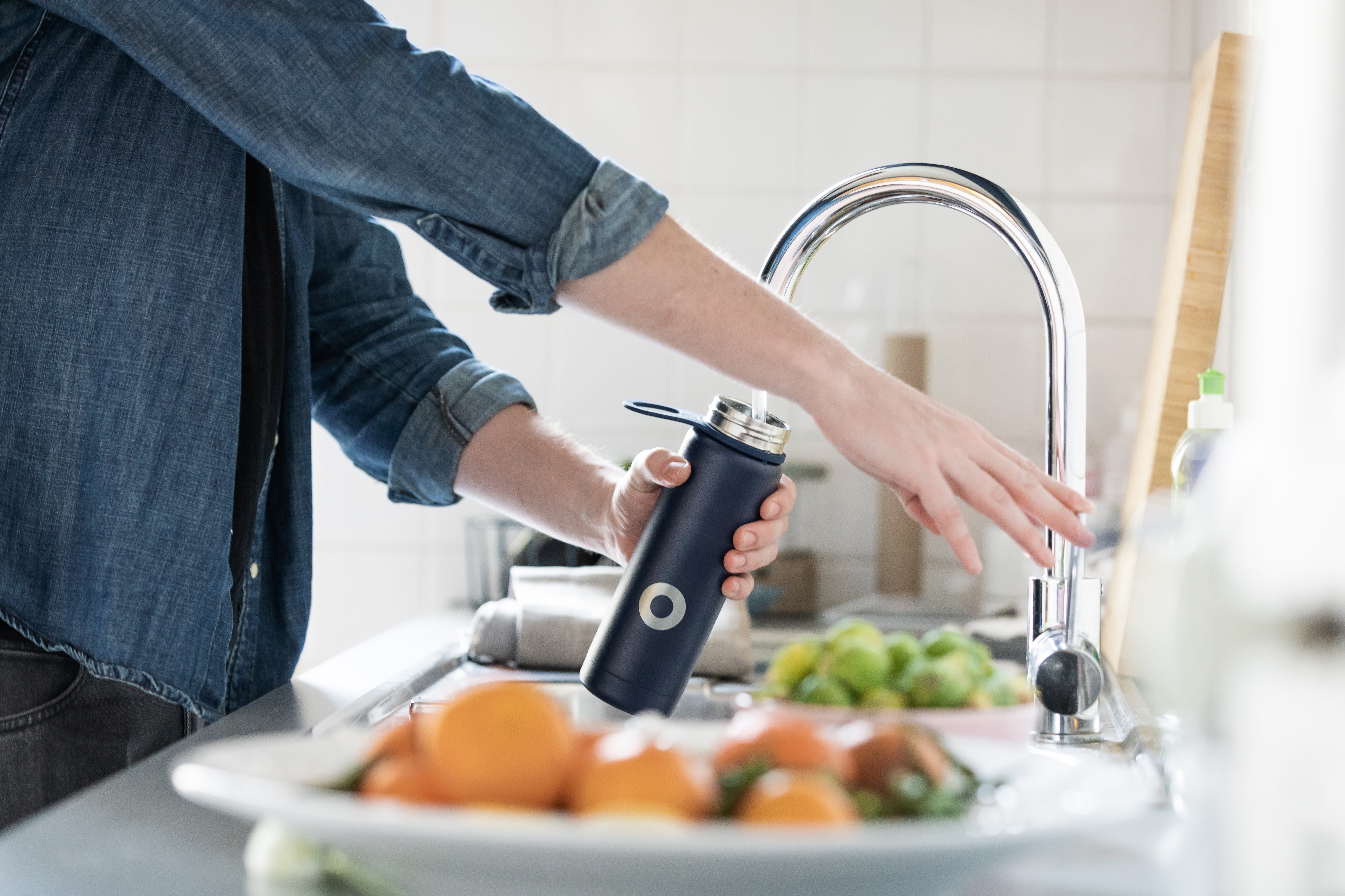 person filling up water bottle at kitchen sink