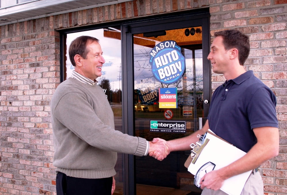 An EGLE employee shakes hands with a local business owner in front of his shop's door