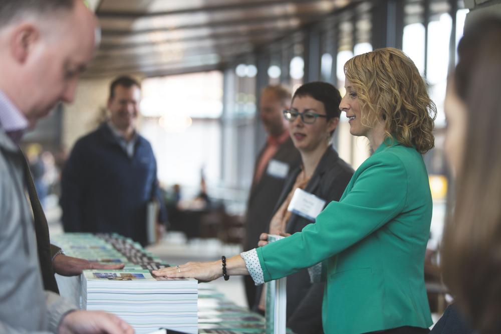 two women behind a table with books and registration materials smiling at man in front of table