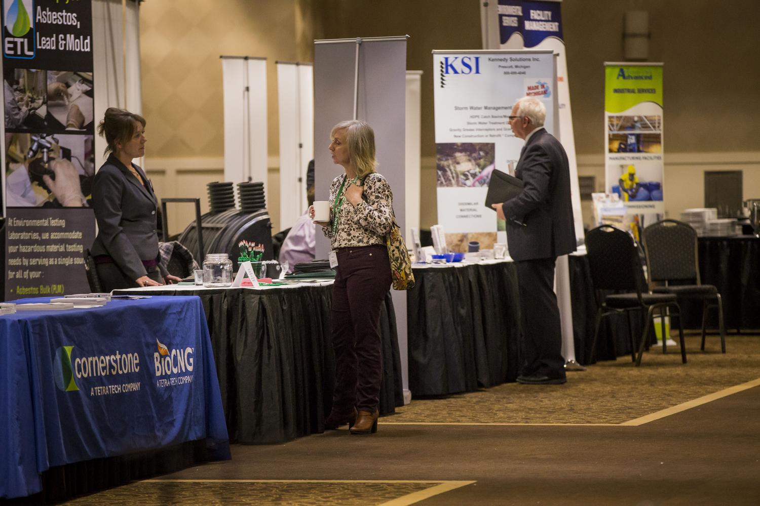 Tables set up at the Waste and Materials Management Conference with several attendees mingling with the hosts
