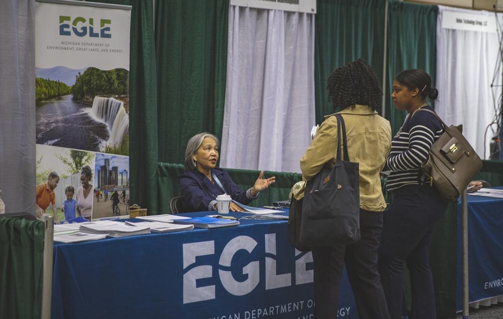 Staff sitting at an EGLE table at an event, handing out brochures to members of the community