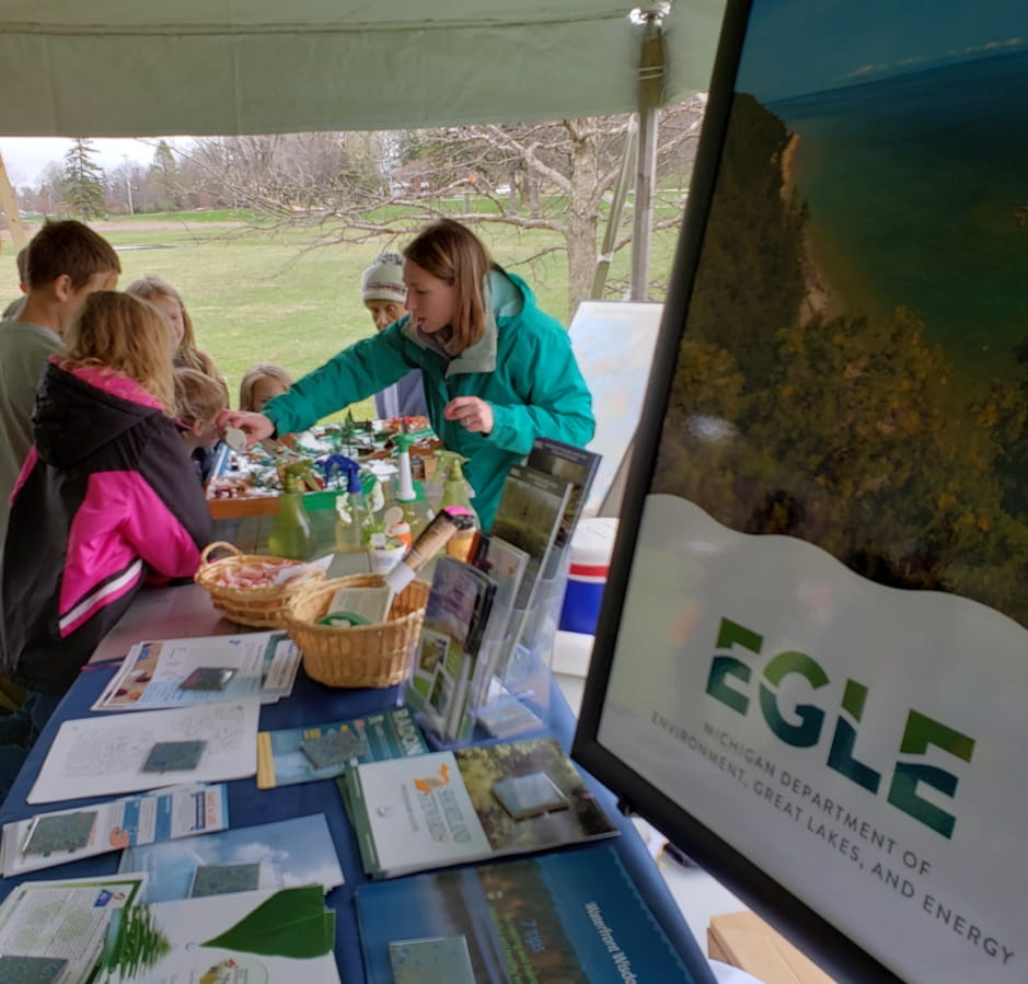EGLE staff talks to kids and adults at display table for Earth Day