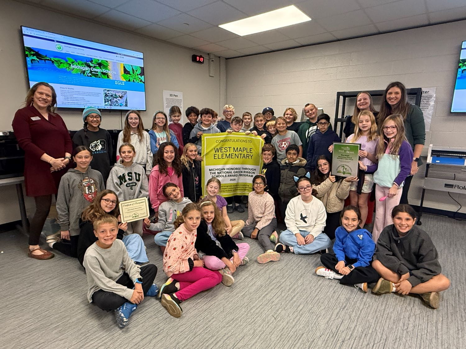A large group of young students smiling and holding up a banner reading Congratulations West Maple Elementary
