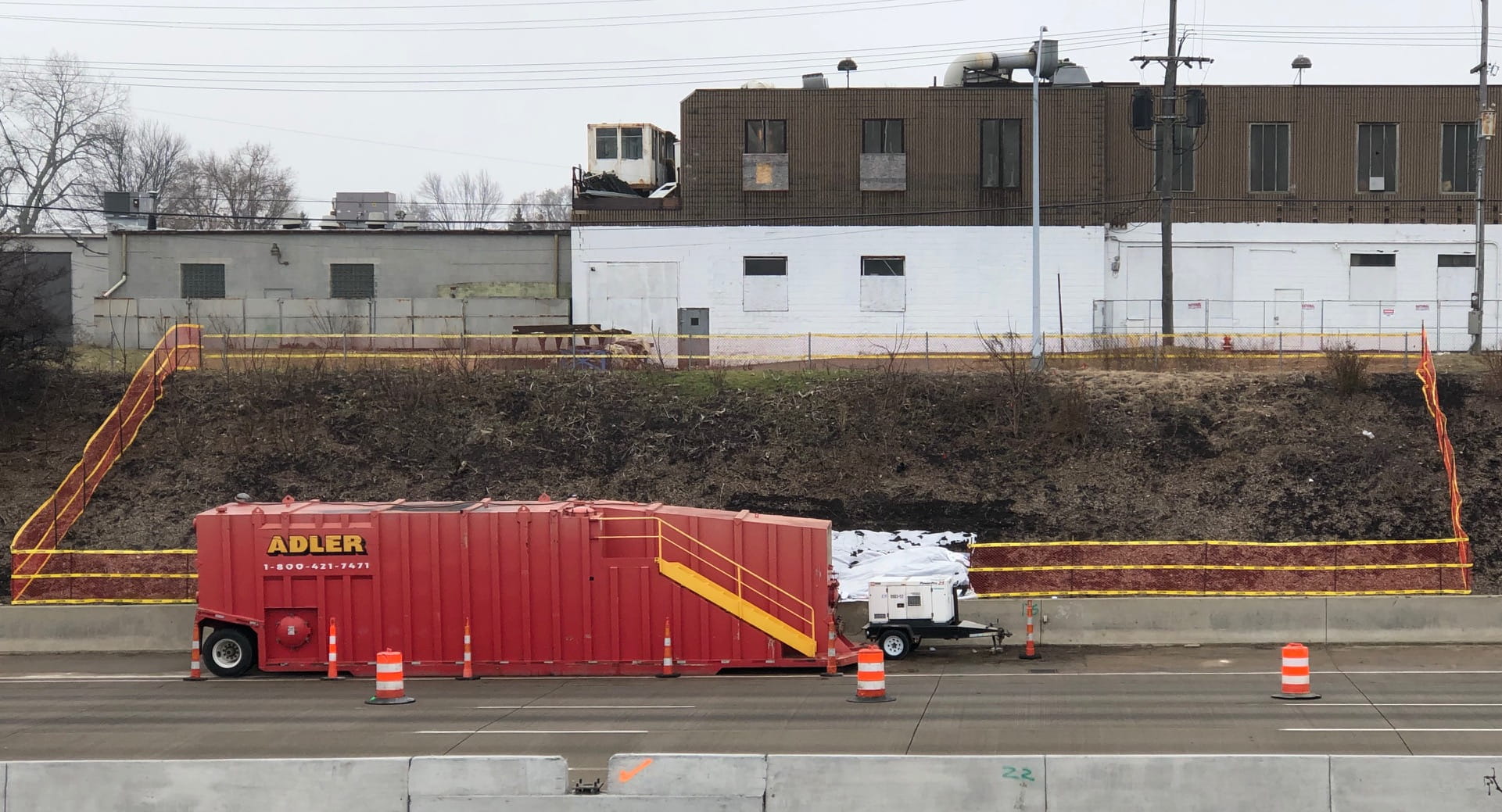 a highway embankment with orange fencing sectioning off the cleanup area with truck in foreground