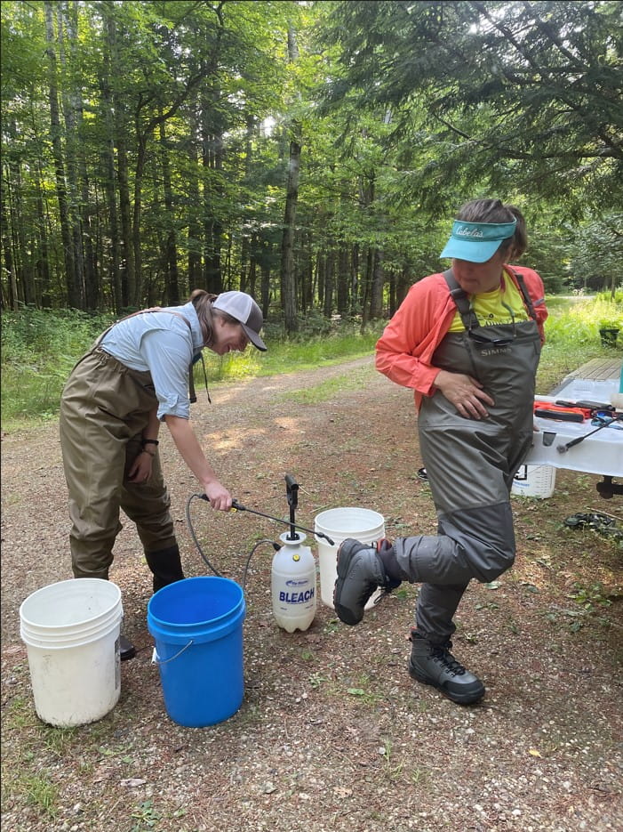 Person cleans waders on another person.
