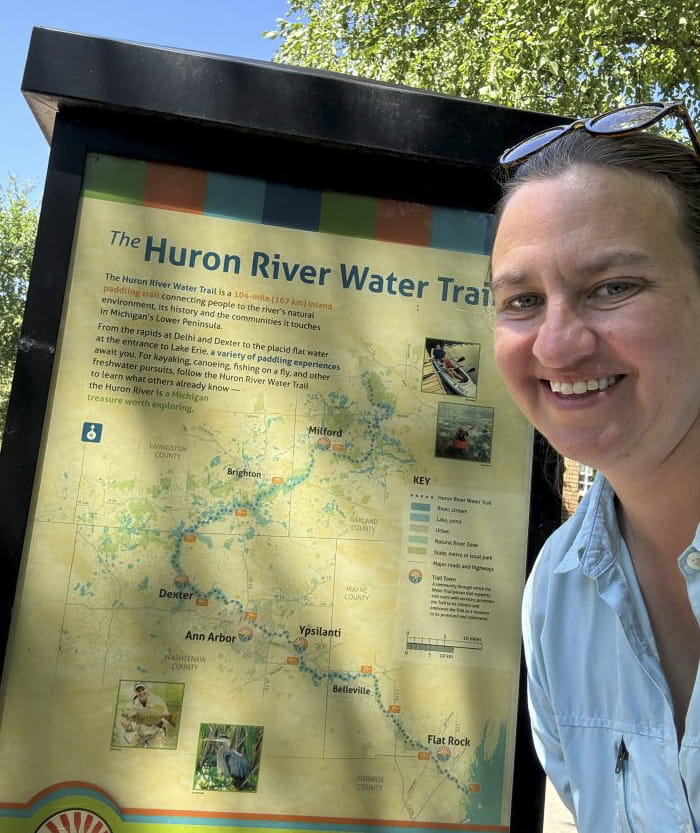 Gillian Gainsley in front of a Huron River Water Trail sign. 