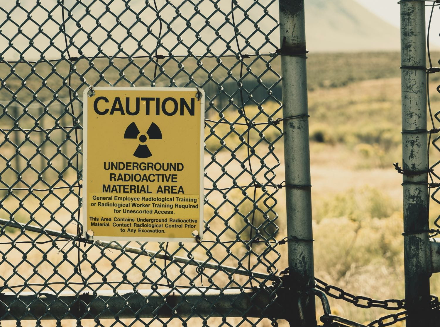 A yellow sign on a chain link fence warning of radioactive materials in the area