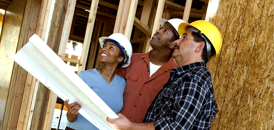 Three construction workers reviewing blueprint for home building.