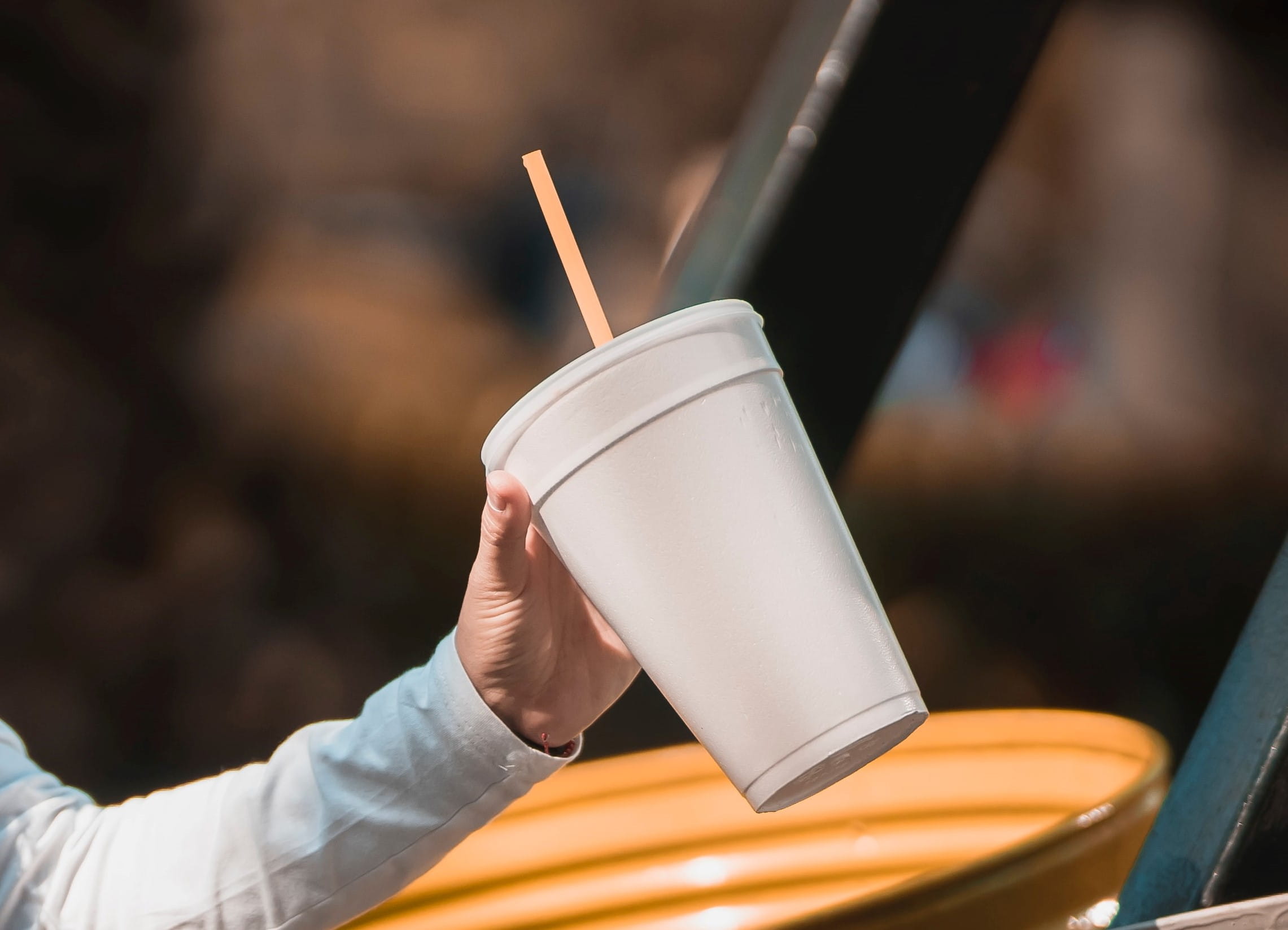 A hand holding out a white Styrofoam drink cup