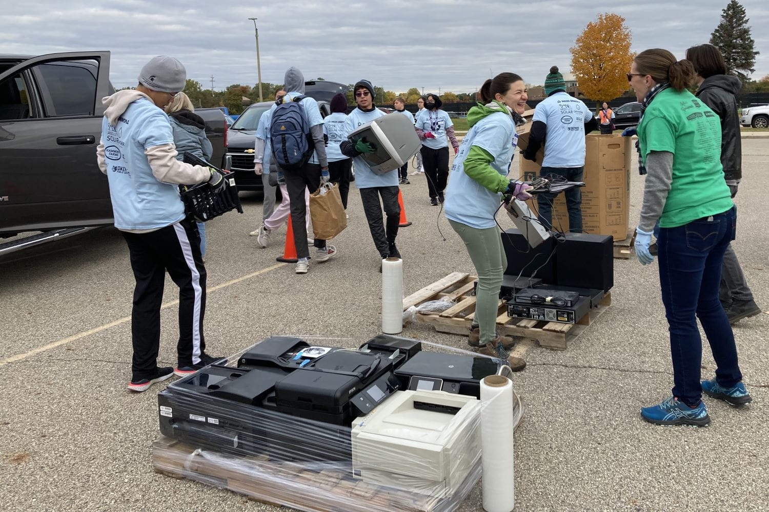 Several volunteers helping stack electronic waste such as computers, TVs, and other electronics into piles at a collection event