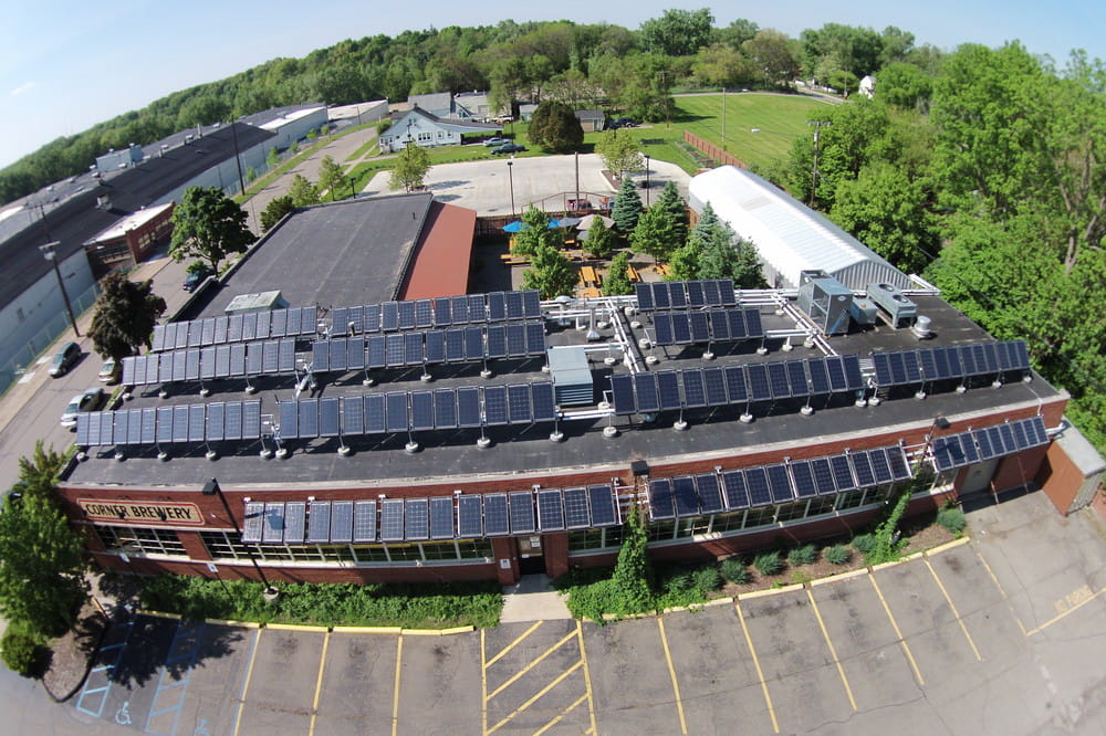 An aerial view of the Corner Brewery in Ypsilanti; it's a brick building surrounded by green trees and the roof is covered in solar panels..