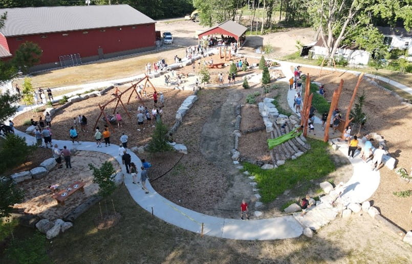 overhead photo of a new playground on a sunny day with people walking around and kids using the equipment.