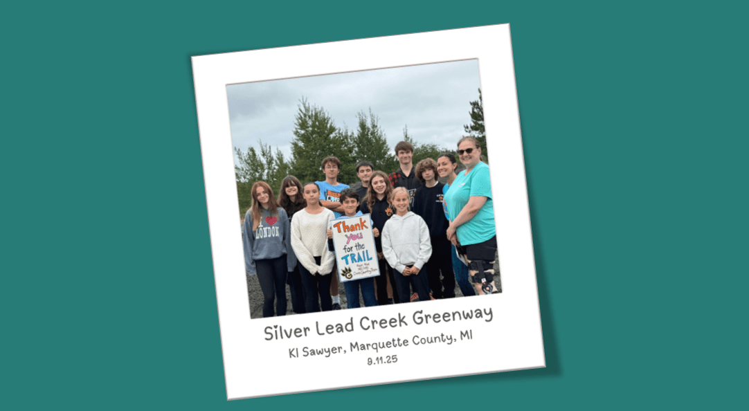 Group of kids outside smiling at the camera holding a thank you for the trail sign