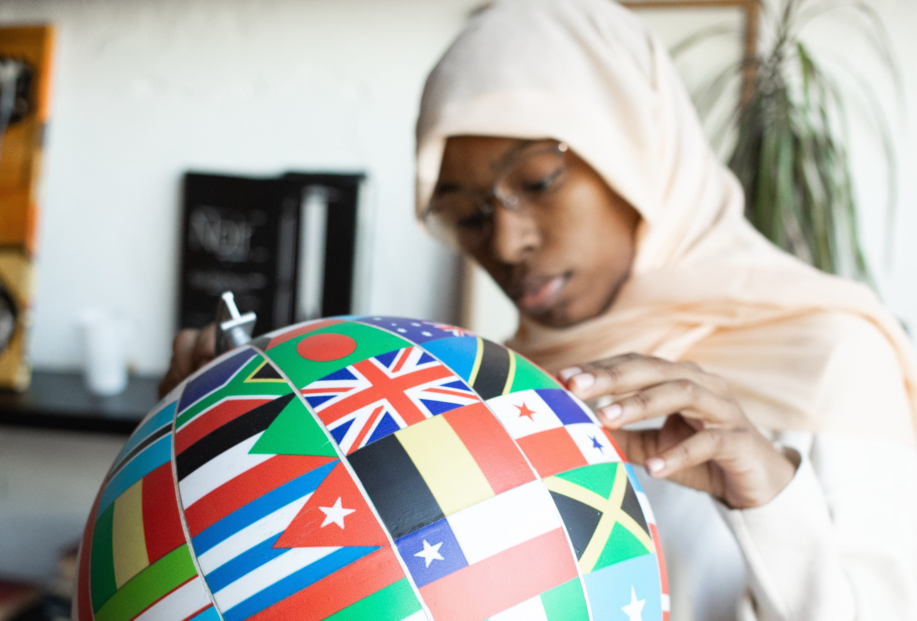 A person wearing a headscarf looking a globe made of world flags