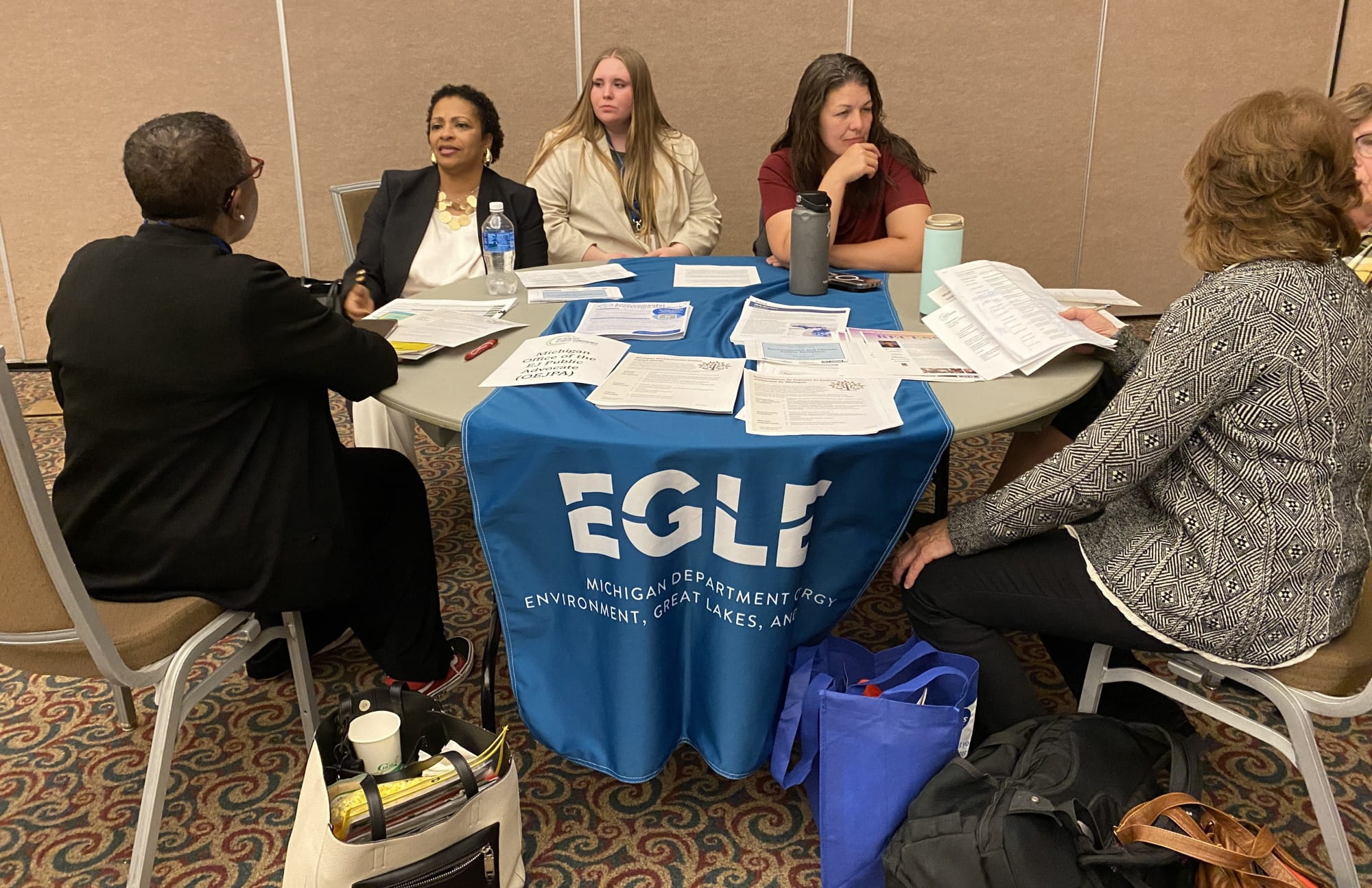 Regina Strong, second from left, and Katie Lambeth, second from right, both with the Office of the Environmental Justice Public Advocate, talk with conference attendees at the Climate Equity Technical Assistance Open House.