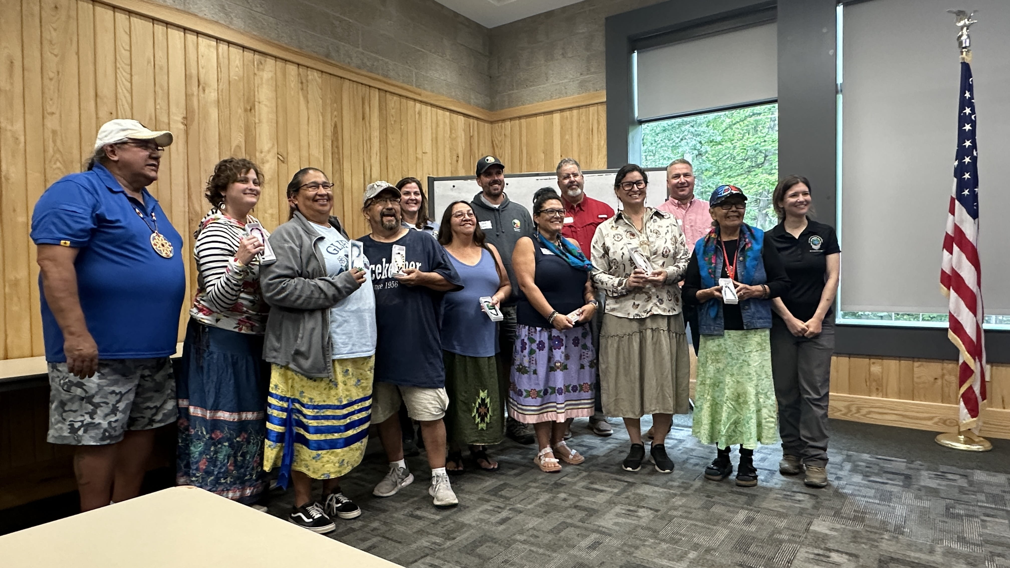 A group of 13 people in a room smiling; some are wearing traditional indigenous clothing