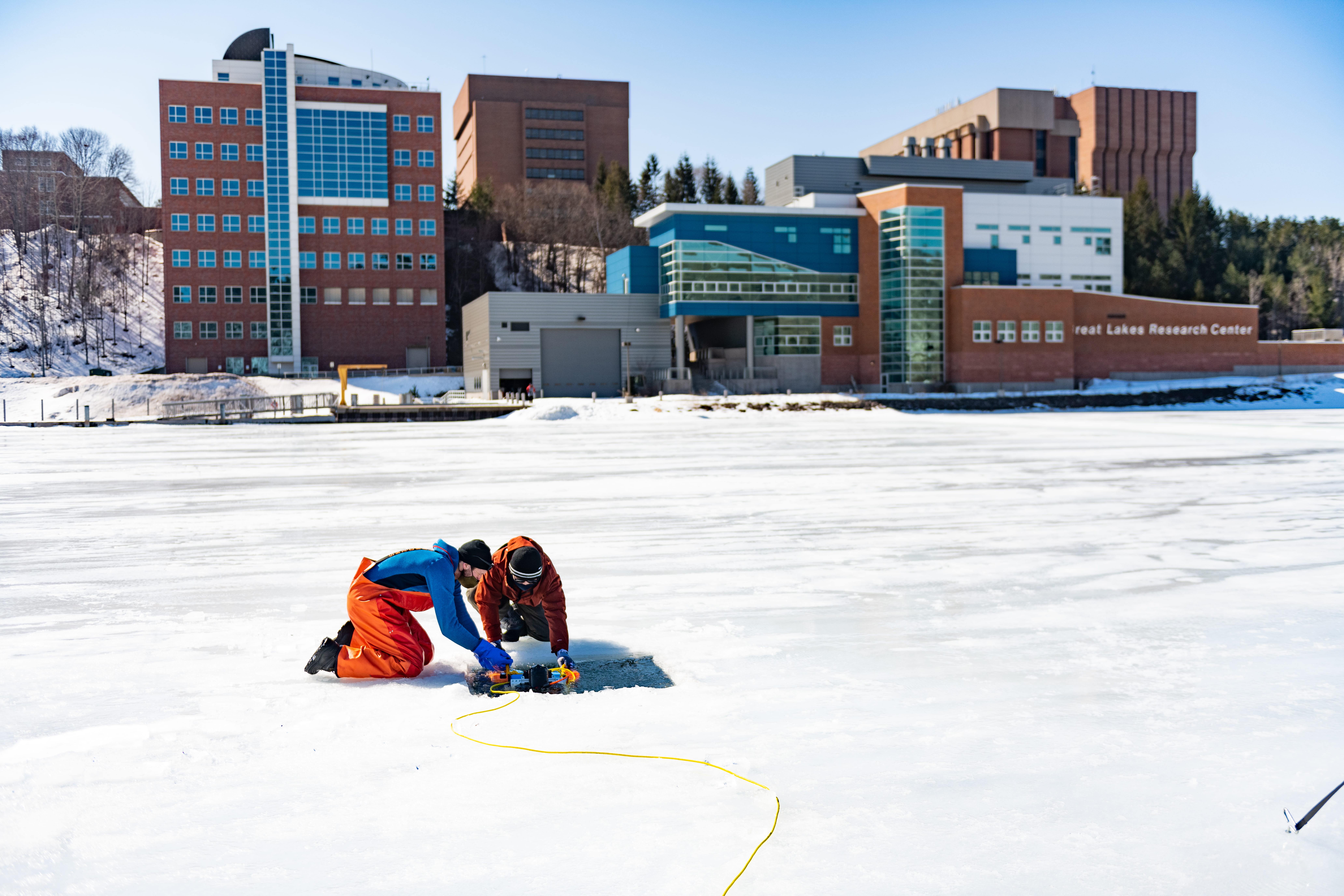  Scientists deploy a remotely operated vehicle (ROV) through the ice in front of Michigan Tech’s Great Lakes Research Center to capture images of the bottom surface of the ice. (Photo courtesy of Michigan Technological University); 