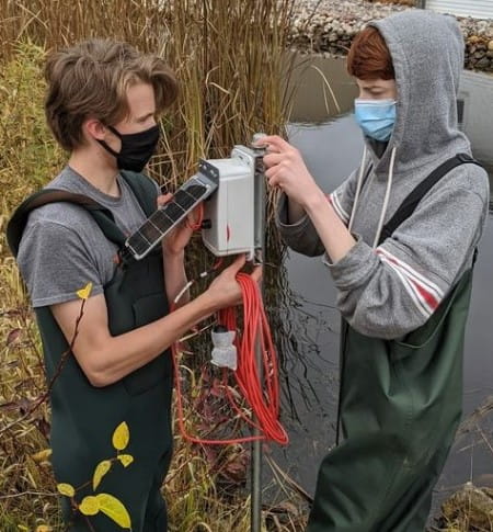 Two students from Les Cheneaux Community Schools district check a solar-powered monitoring station 