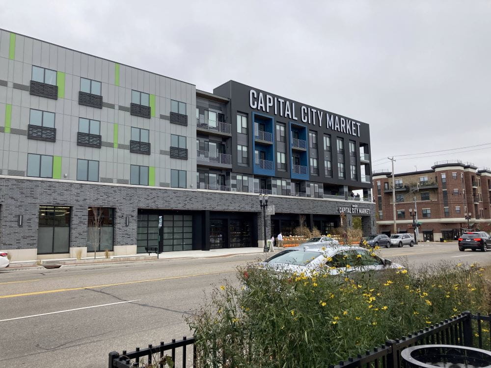 A four story building on a street corner in downtown Lansing; the sign reads Capital City Market