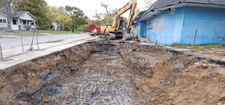 An excavator sits at the end of a hole where contaminated soil and an underground storage tank were removed.