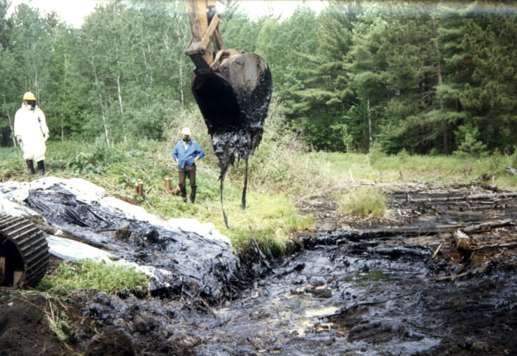 An excavator removing black sludge from a creek