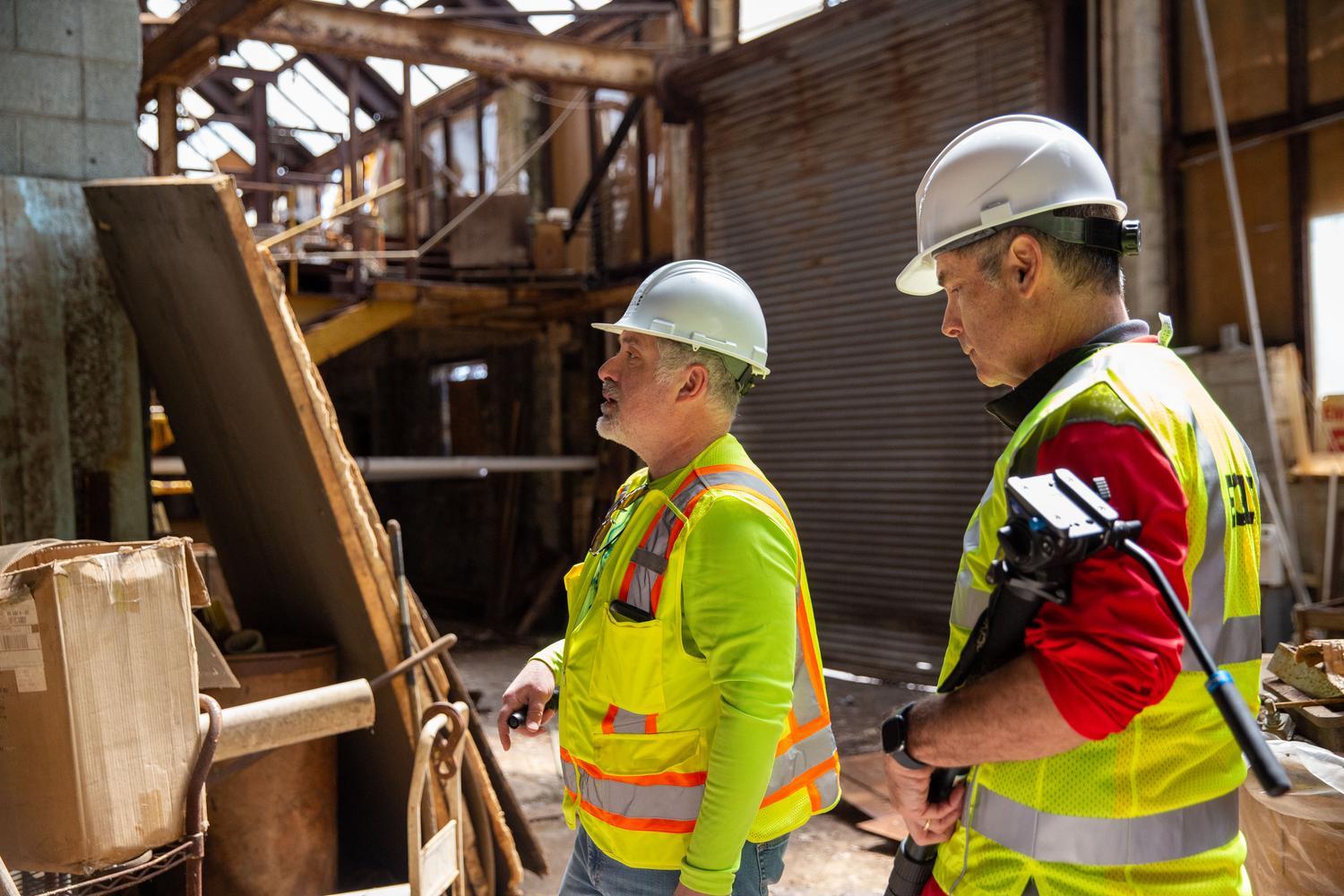 Two EGLE staff wearing yellow construction vests and hardhats look onwards to the demolition job before them