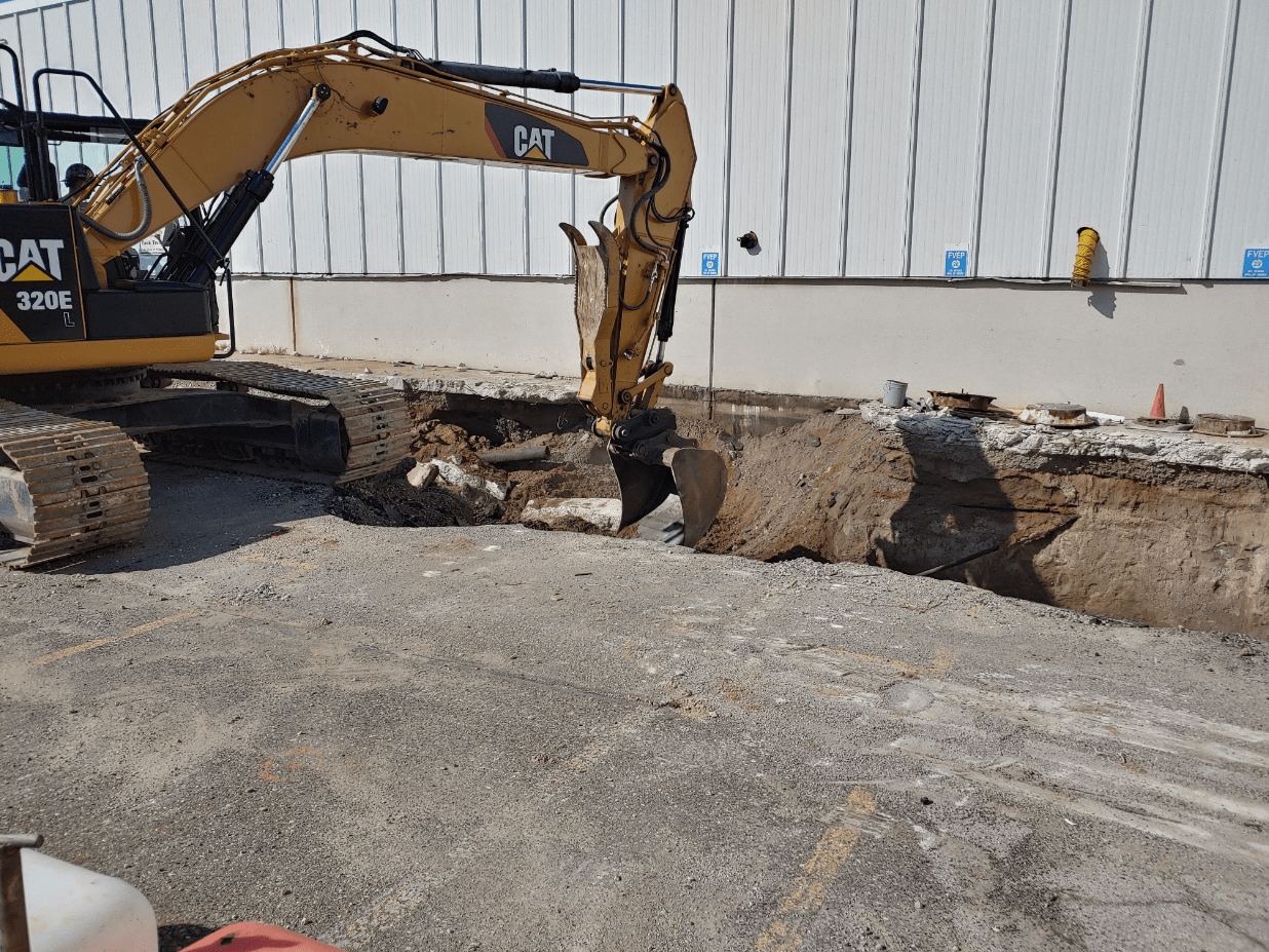 An excavator next to a large hole in a concrete parking lot