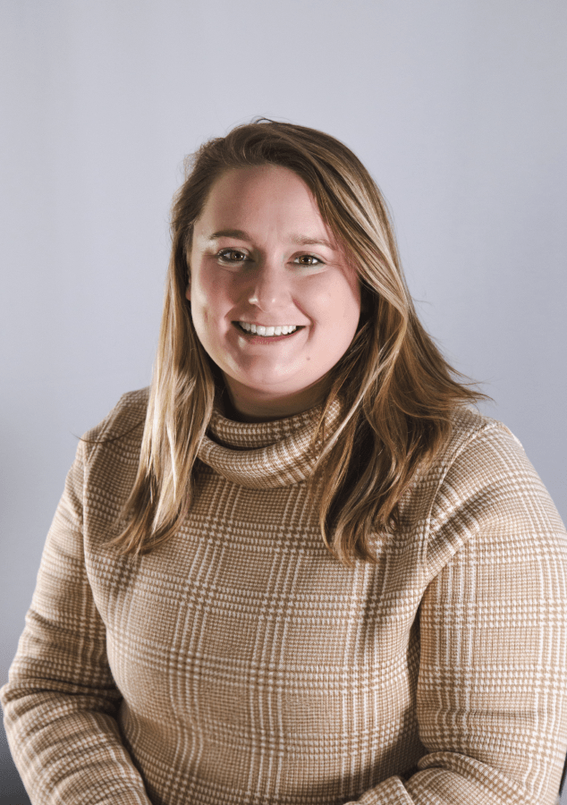 Sydney Hart, in a patterned brown turtleneck, smiling
