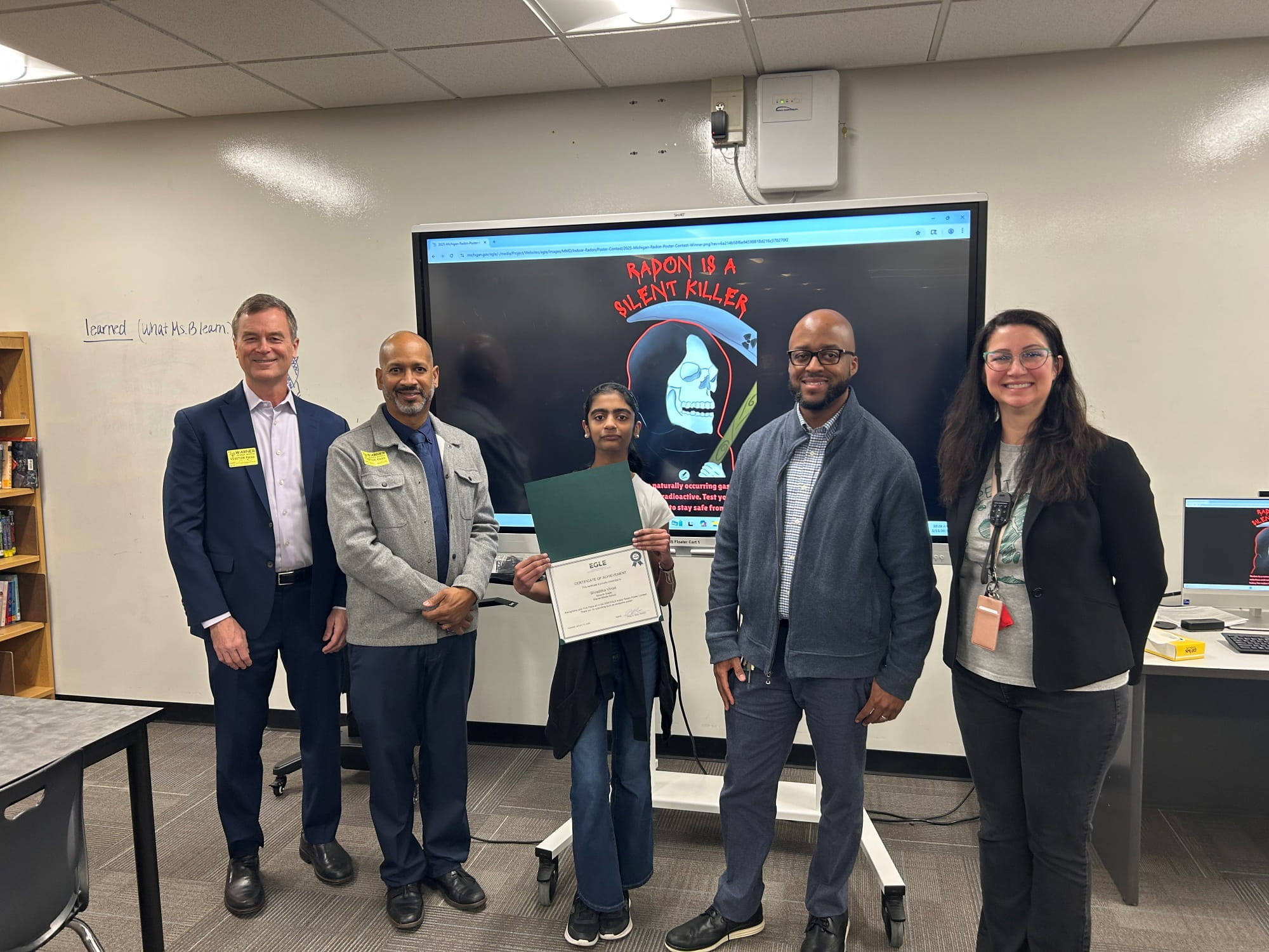 EGLE Director Phil Roos and EGLE Indoor Radon Specialist Leslie Smith III present a certificate to Shraddha Vinod, the radon poster contest winner, at Warner Middle School in Farmington Hills.