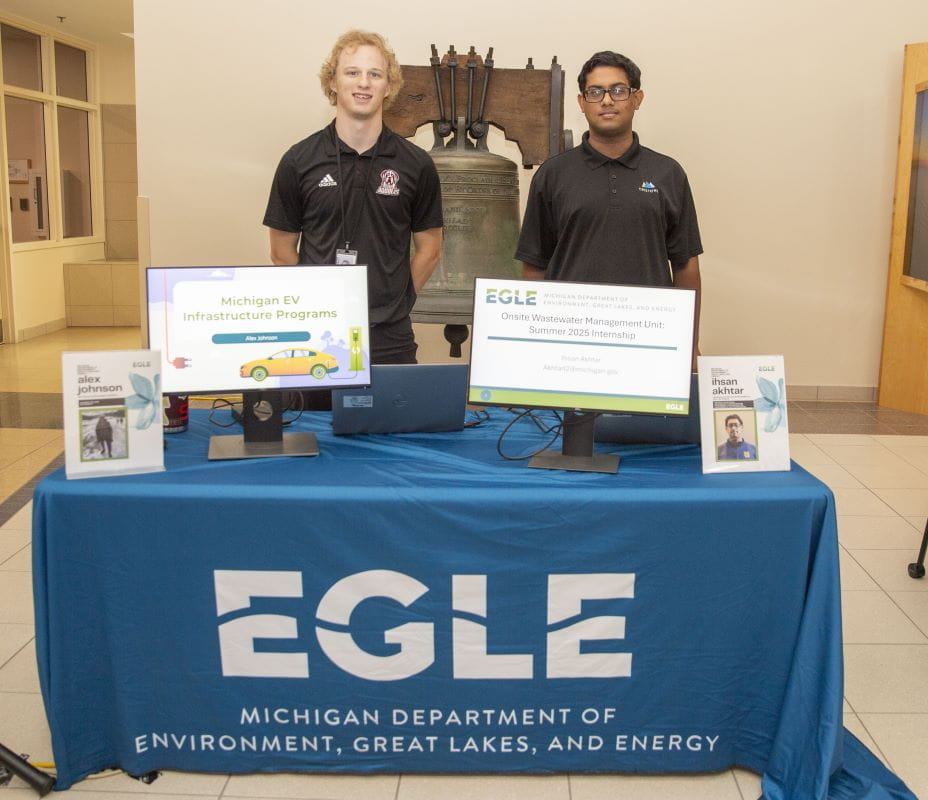 Alex Johnson and Ihsan Aktar are interns at a EGLE table, the table has computer screens showing Michigan EV and internships.