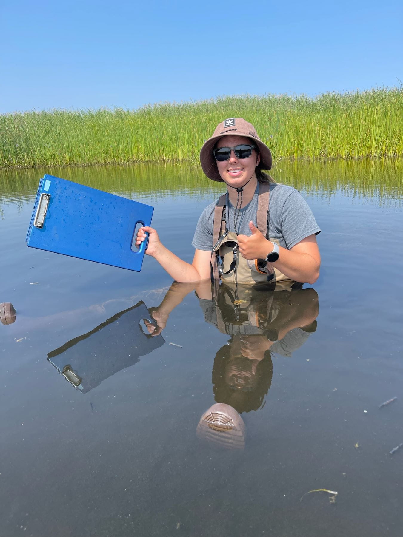 EGLE staffer Alex Adams-McDevitt in the water holding clipboard.
