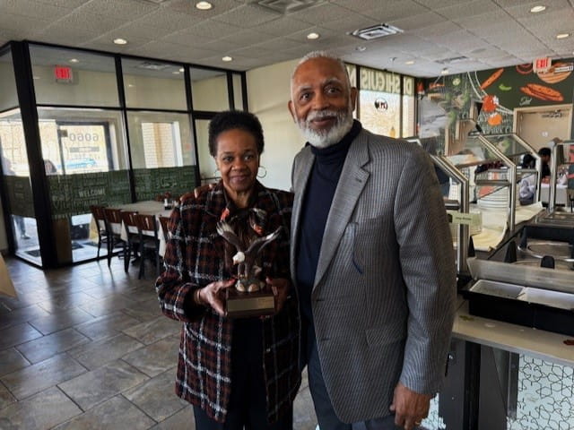 Sandra and her husband Bill posing for a photo smiling and holding the hand-carved eagle statue award