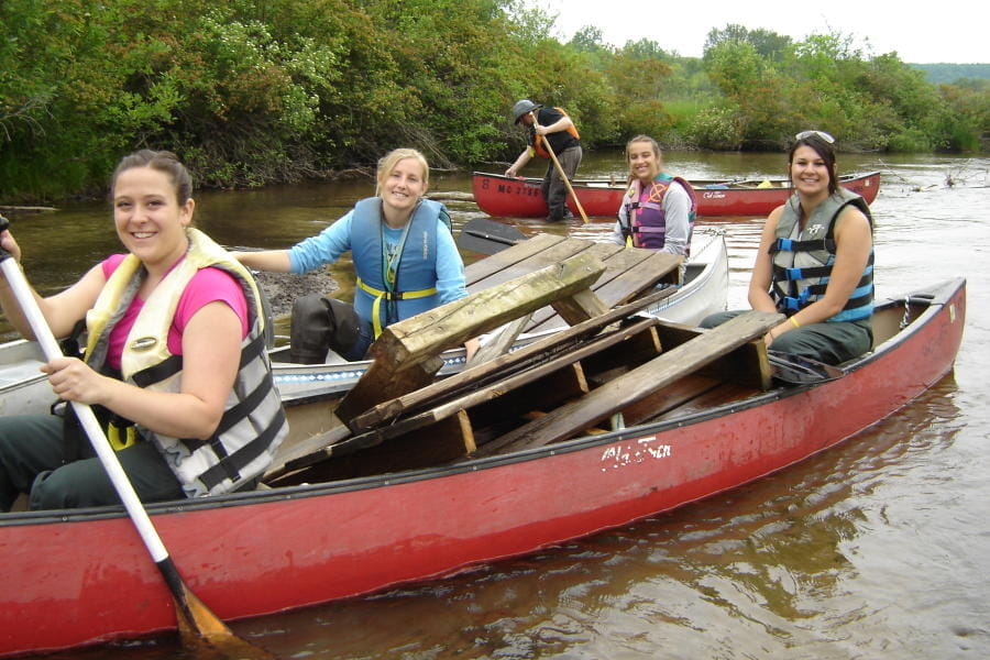 MI Corps volunteers in two canoes clean up a river. 