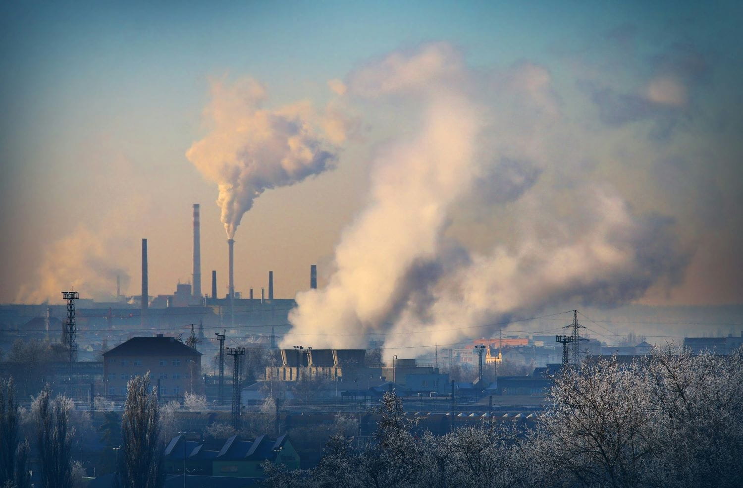 A large industrial factory with multiple smokestacks emitting  a thick white smoke into the air