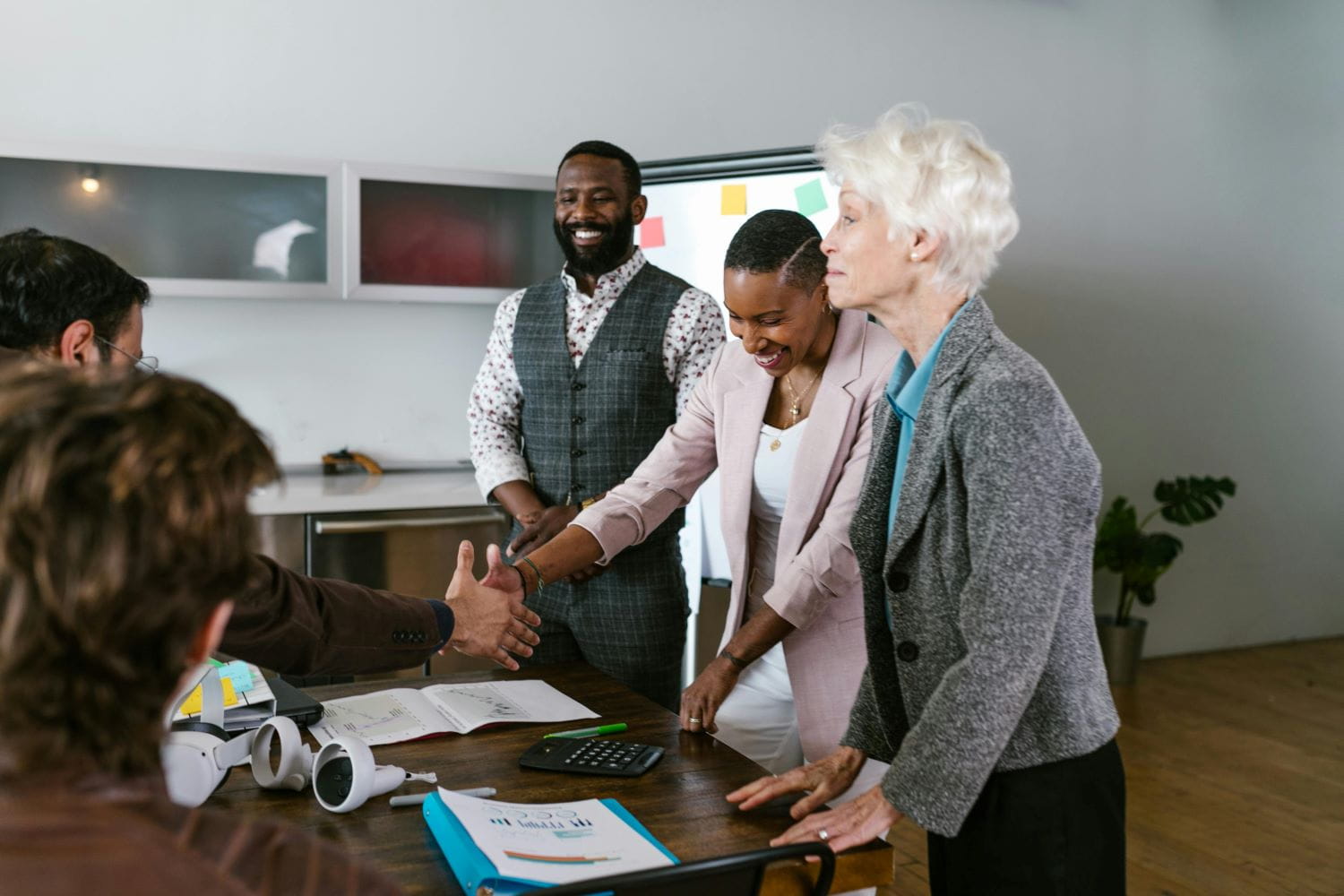 Five diverse business partners lean over a desk and shake hands
