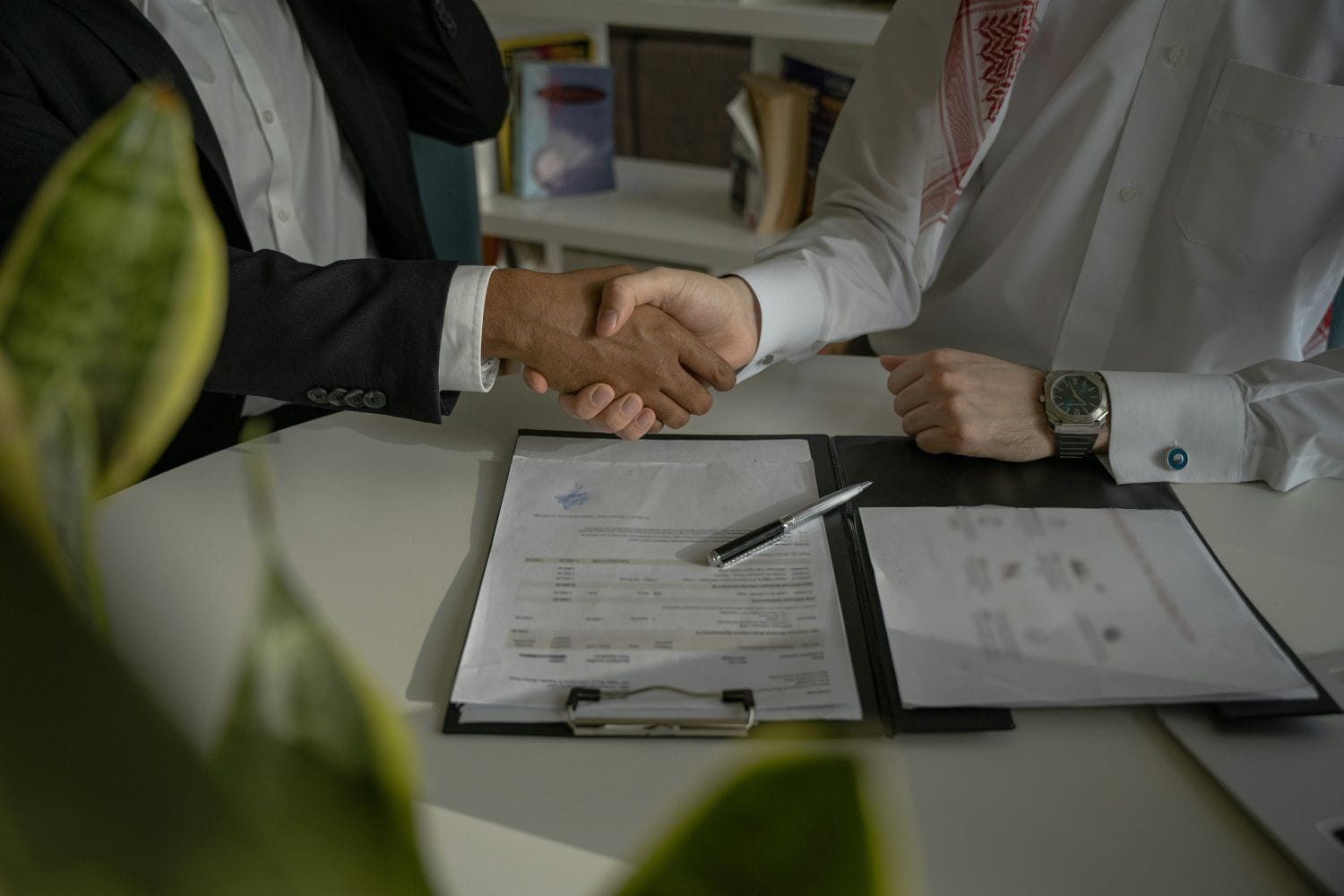 Two people in business attire shaking hands over a contract laid out on a desk