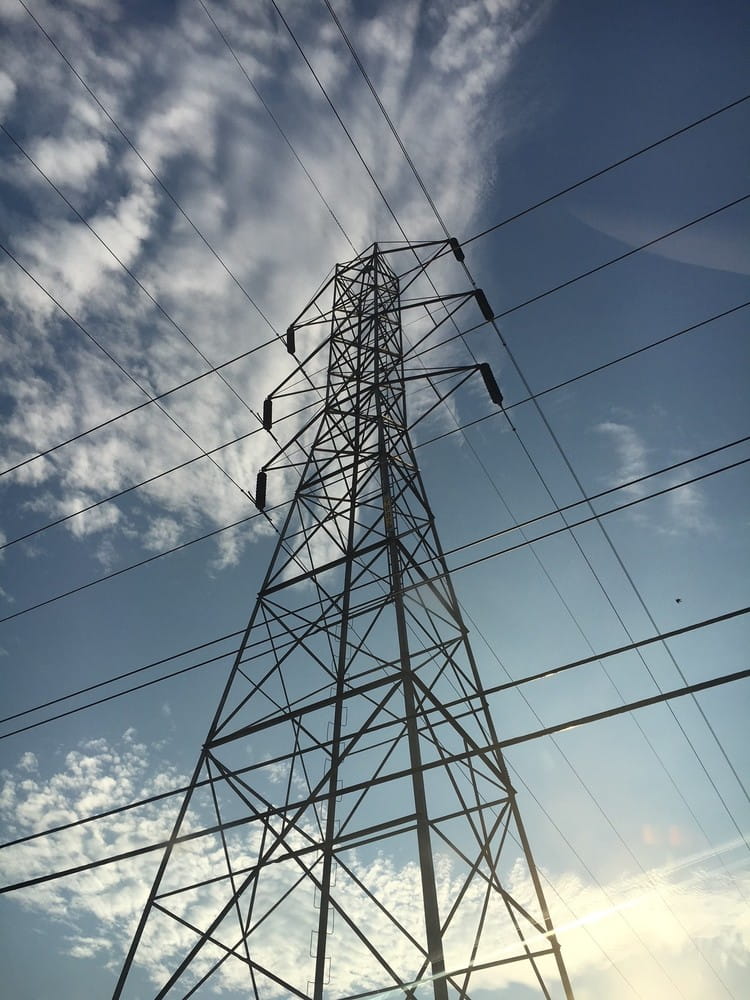 Looking up at an enormous electrical tower, against a blue sky