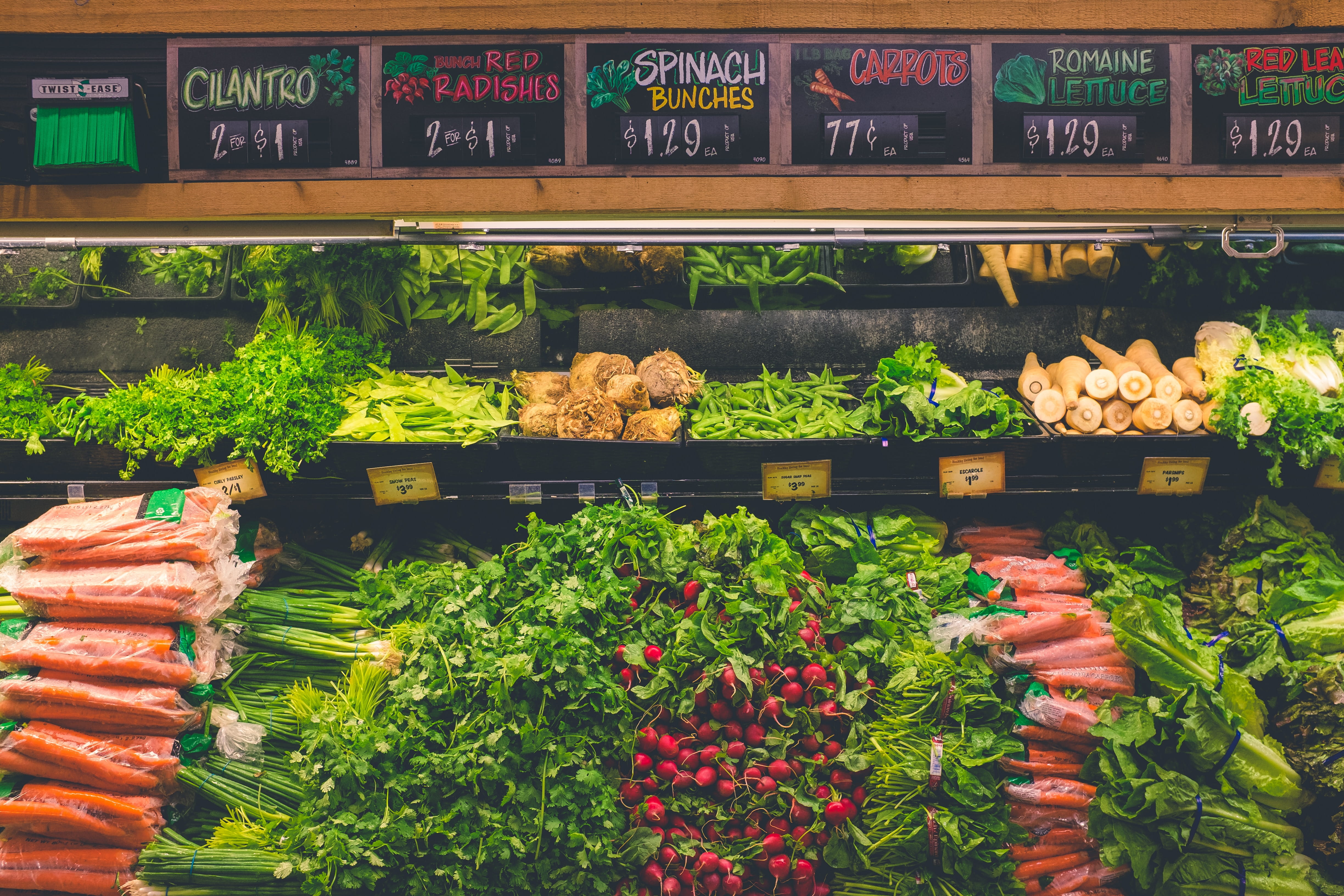 The produce section at a grocery store; carrots, beets, green onions, and other vegetables stacked neatly beneath price signs