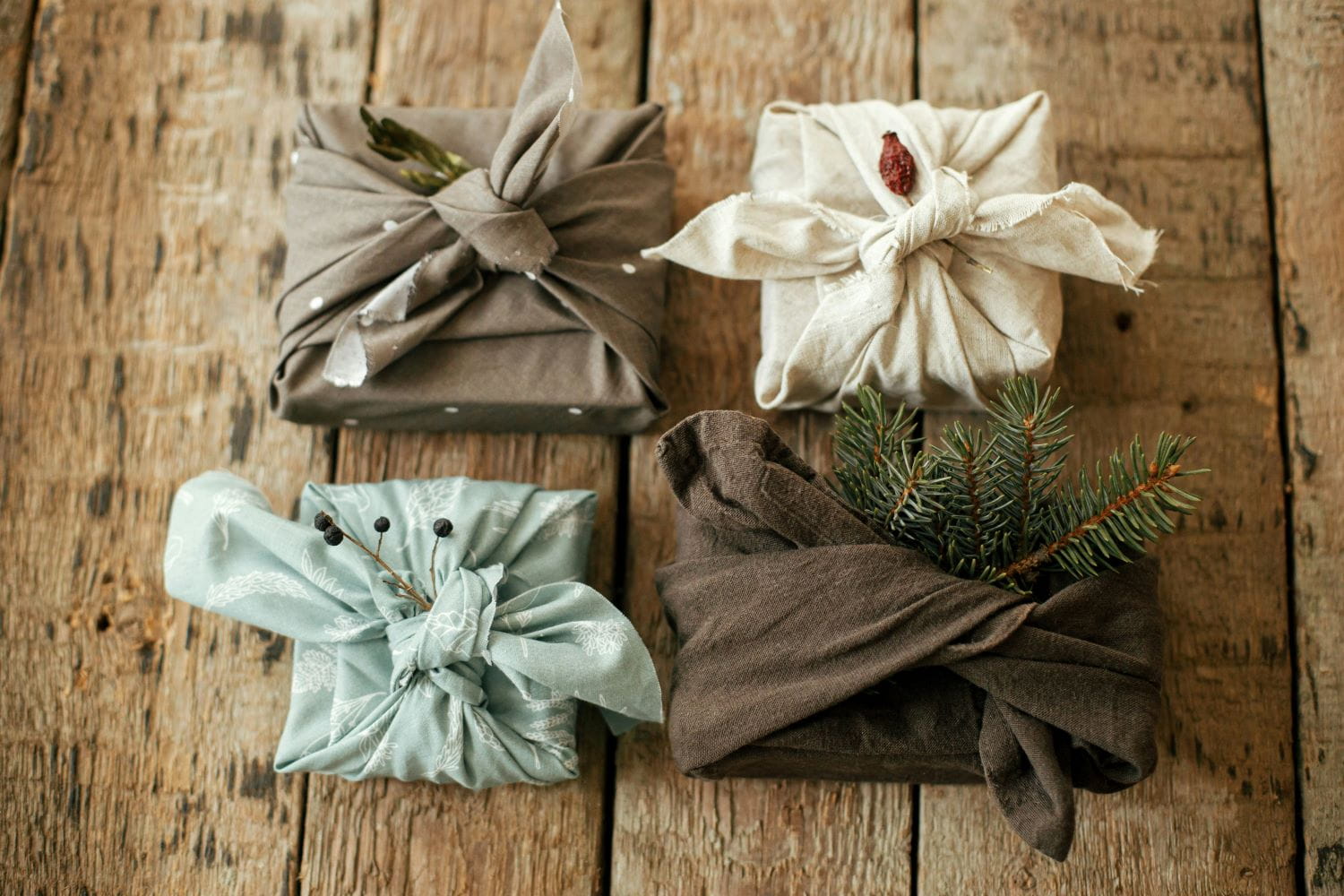 Four gifts wrapped in reusable cloth giftwrap, adorned with sprigs of spruce